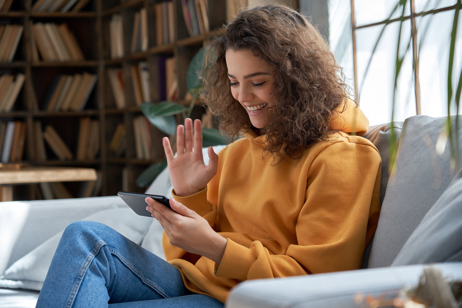 Happy hispanic girl sit on sofa hold phone video calling online in mobile app.