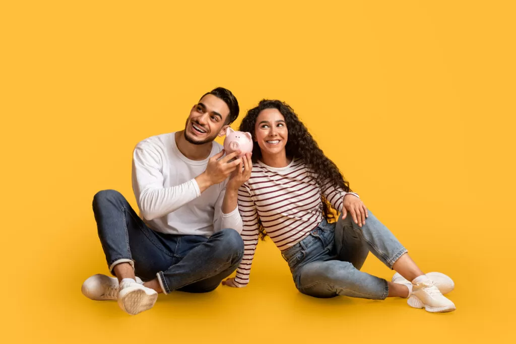 A couple sitting down holding a piggy bank in front of a yellow background in Chicago.