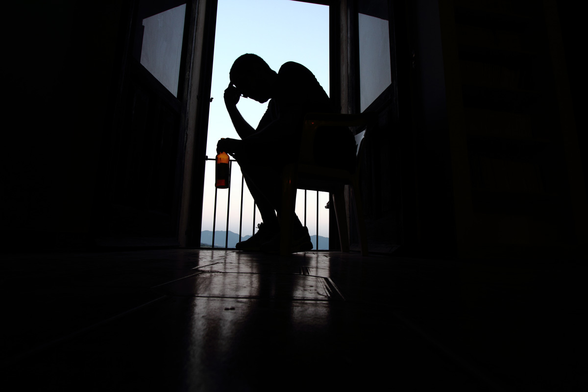 A person sitting in a chair with their head in their hand and holding a bottle of alcohol in Chicago.